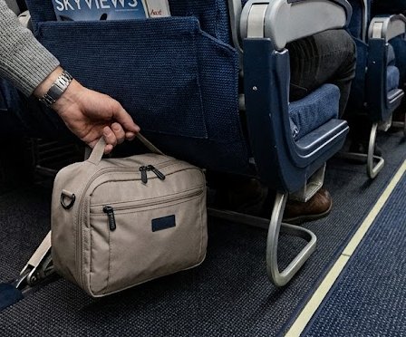 Passenger putting a small bag under a economy aircraft seat